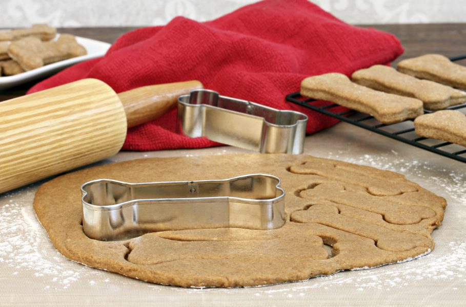 Dog biscuit dough with rolling pin and bone shaped cookie cutters on a silicone mat.